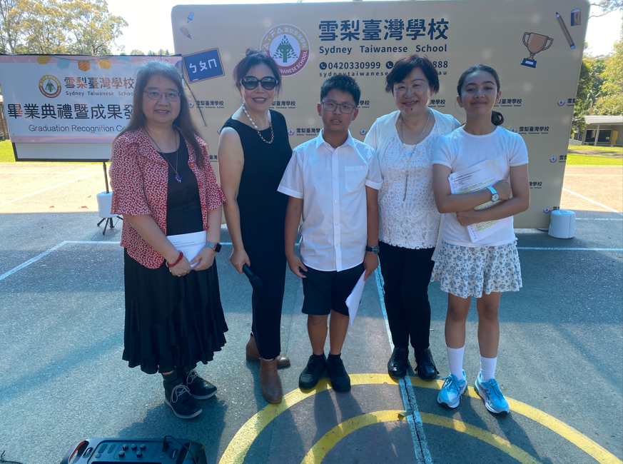 校長劉碧珍博士、榮退的蔣秋蓮老師、六年級畢業班的導師陳啟鈺老師和中英文主持人許維畯、黃宇韻同學在舞臺前合影