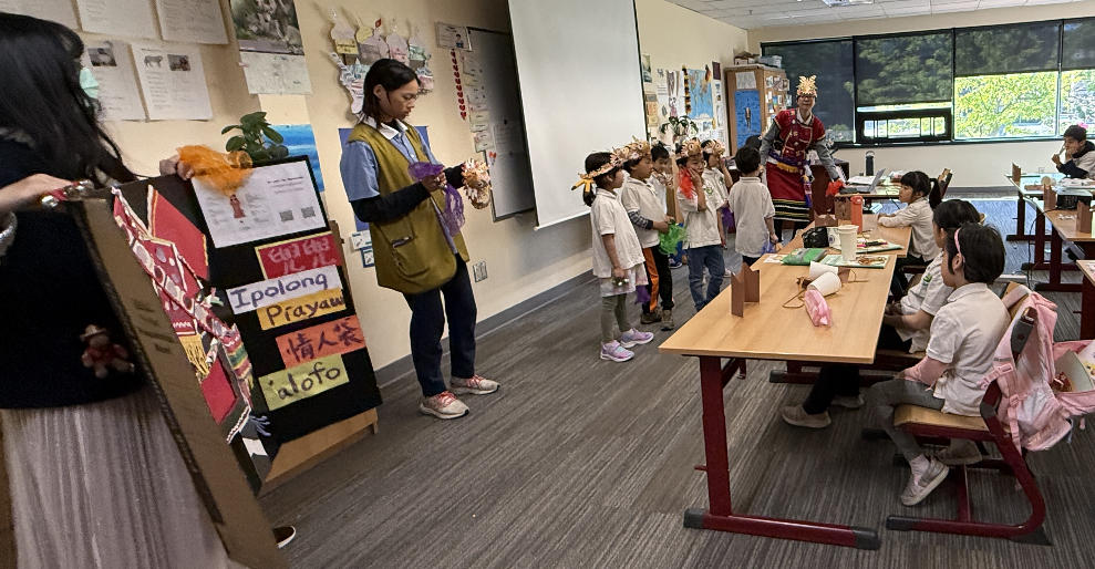家長志工拿著看板讓賴筱雯為學生解說阿美族傳統服飾特色。