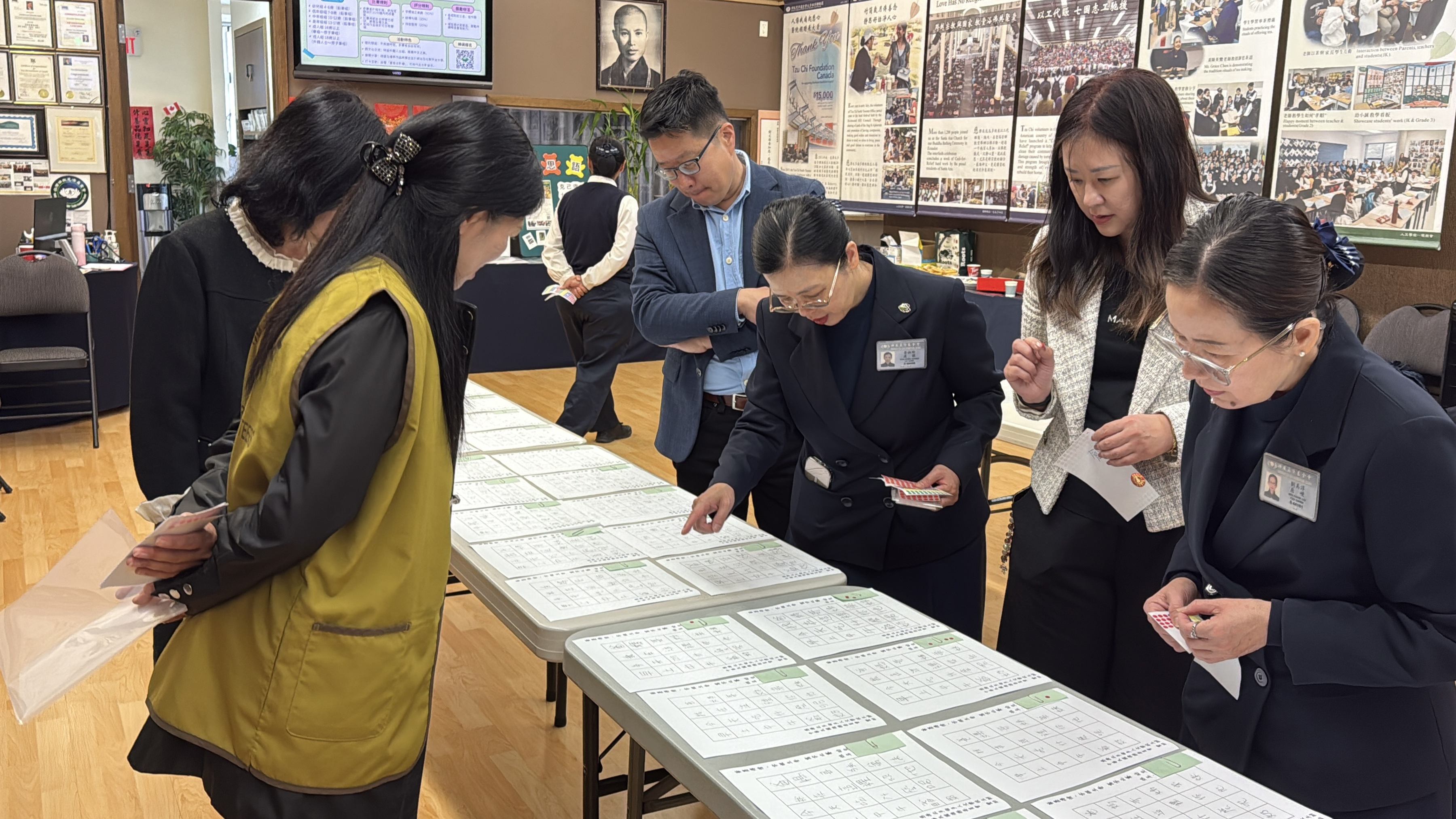 四位評審專注地逐一審閱參賽作品，秉持公平、公正、公開的原則進行評分。駐多倫多臺北經濟文化辦事處文化中心主任藍柏青及副主任許彩鳳等貴賓與志工們也在旁觀摩，讚賞參賽者們用心書寫的佳作。攝影者：梁延康 