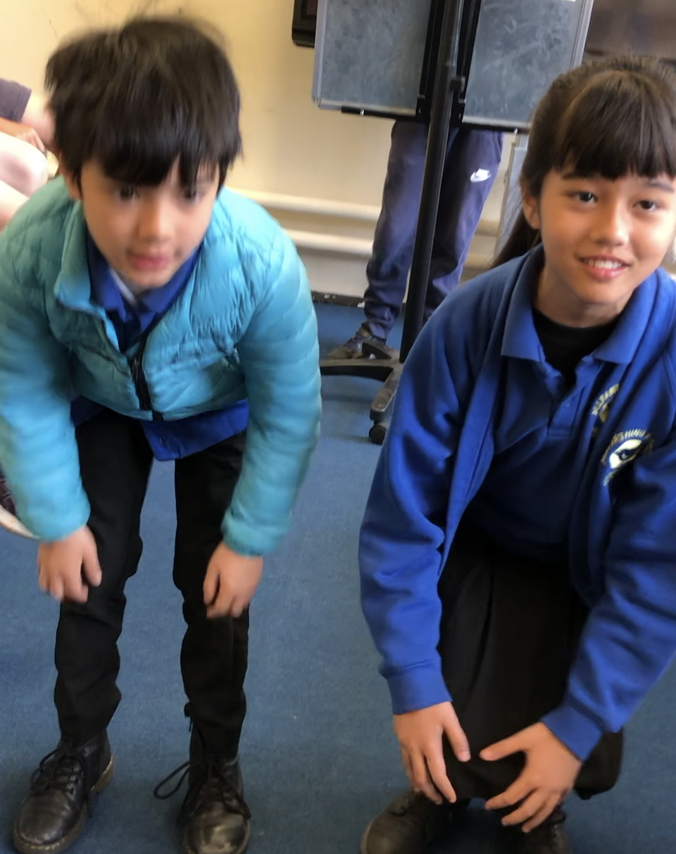 兩個孩子，他們正在參加一個歌唱比賽。孩子們穿著學校的校服，站在教室裡，做著配合歌唱的動作。他們的表情專注且充滿熱情，顯示出他們對比賽的投入和興奮。